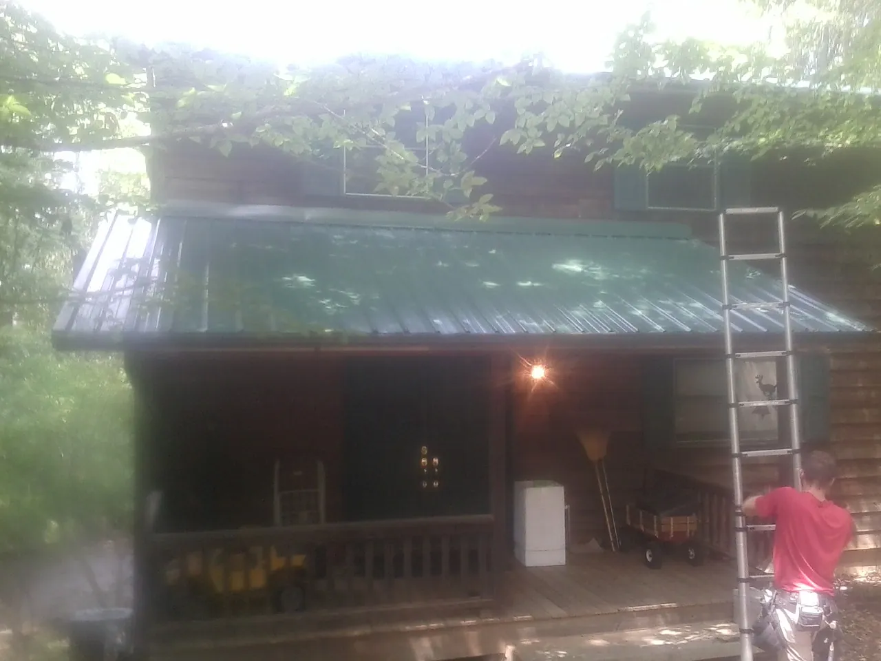 Worker on a ladder at the green porch roof of a wooded cabin in Auburn